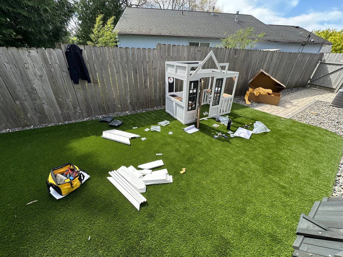 Playhouse panels and parts spread across a backyard lawn mid-assembly