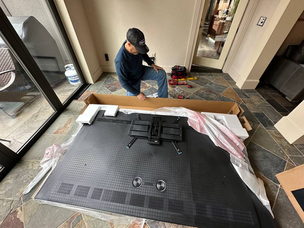 Large TV face down on a drop cloth with the wall bracket being fitted